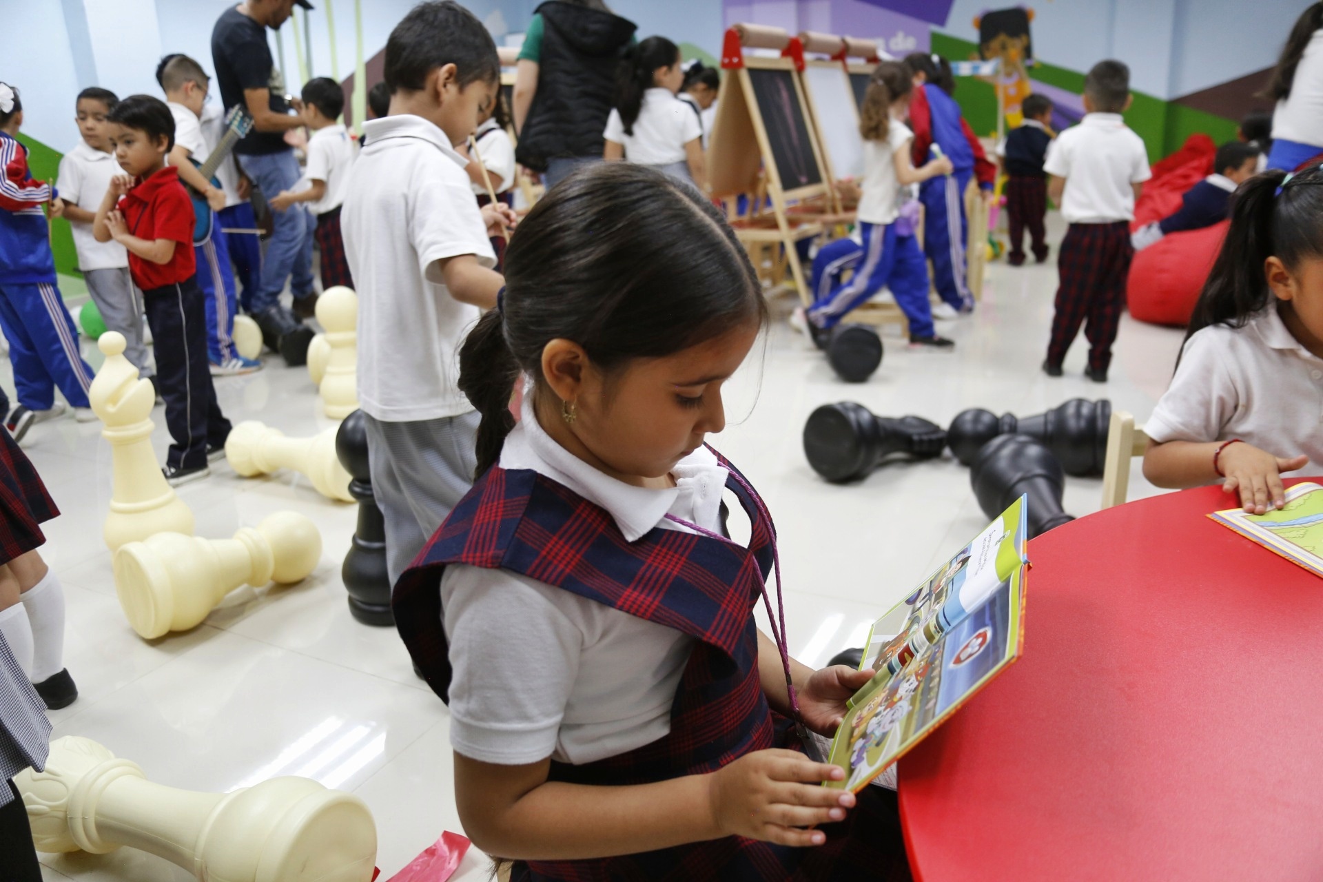 Niña leyendo un libro al fono más niños jugando